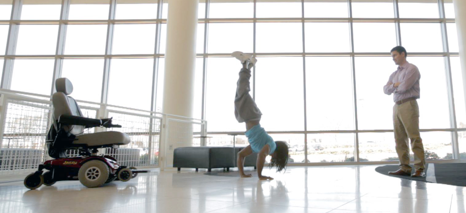 Zarius Walker – out of his wheelchair – does a handstand while a man looks on.